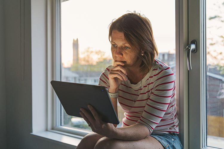 Woman using digital tablet on window sill